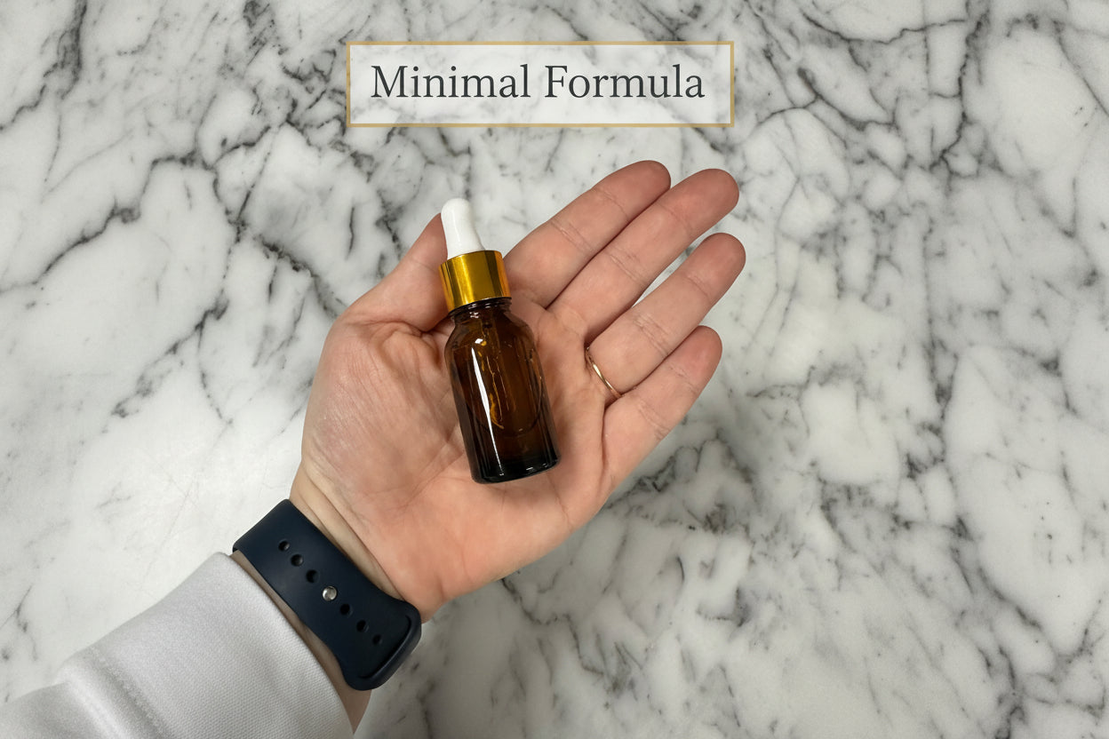 Hand holding a small brown glass bottle with a dropper against a marble background