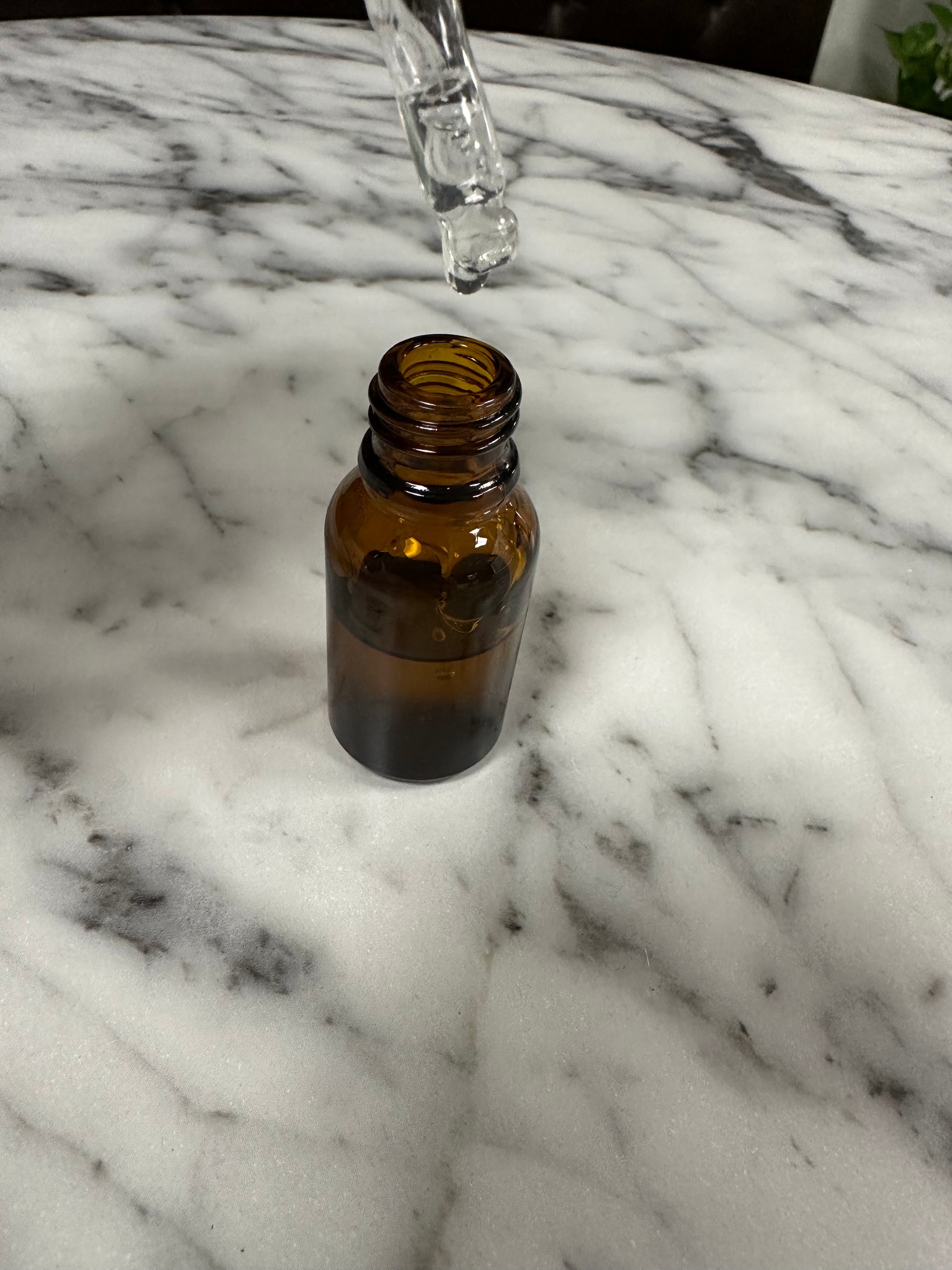 Brown glass bottle on a marble surface with a dropper above it.